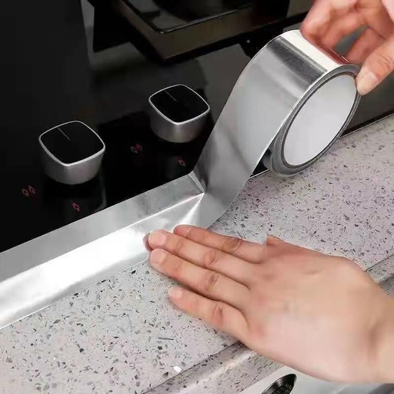 Person applying silver sealing tape to a kitchen countertop.